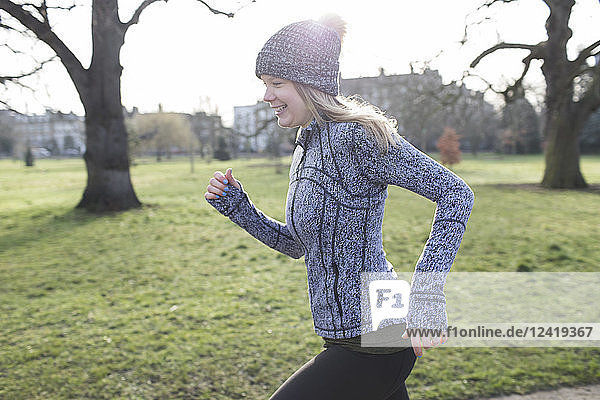 Smiling female runner running in sunny park