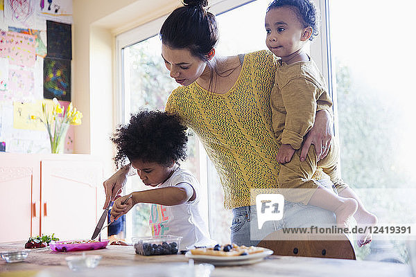 Mutter hilft ihrer kleinen Tochter beim Schneiden von Frühstückswaffeln