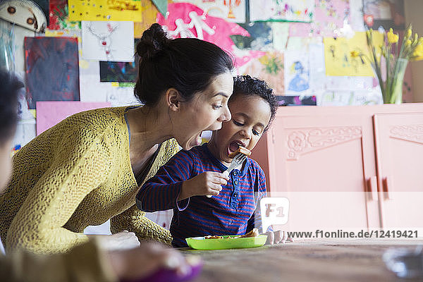 Verspielte Mutter und Sohn essen Frühstückswaffeln am Tisch