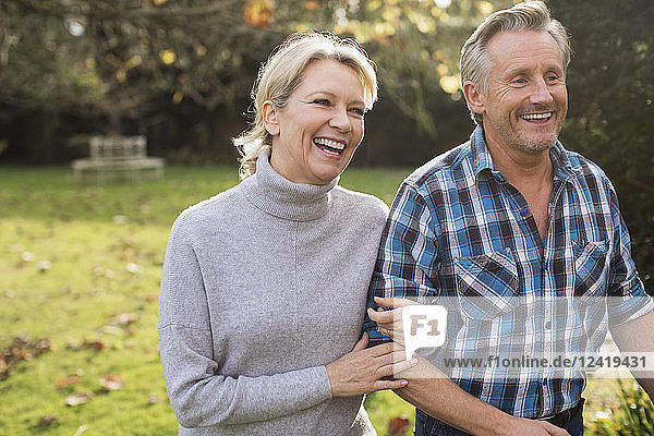 Happy  carefree mature couple walking arm in arm in sunny autumn park