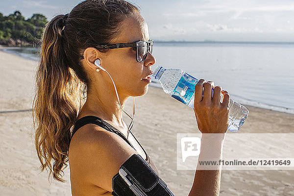 Thailand  Koh Phangan  Sportive woman drinking water on the beach