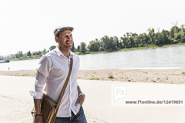 Mature man wearing flat hat at Rhine riverbank