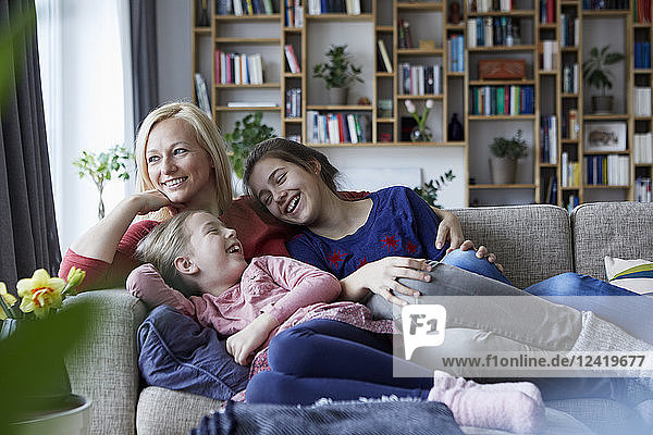 Mother and her daughters cuddling and having fun  sitting on couch