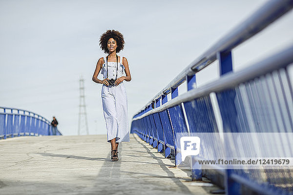 Content young woman with camera walking on a bridge