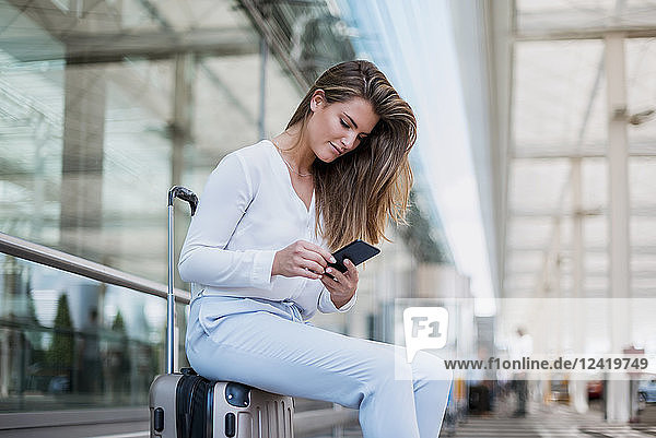 Young businesswoman sitting outdoors on luggage using cell phone
