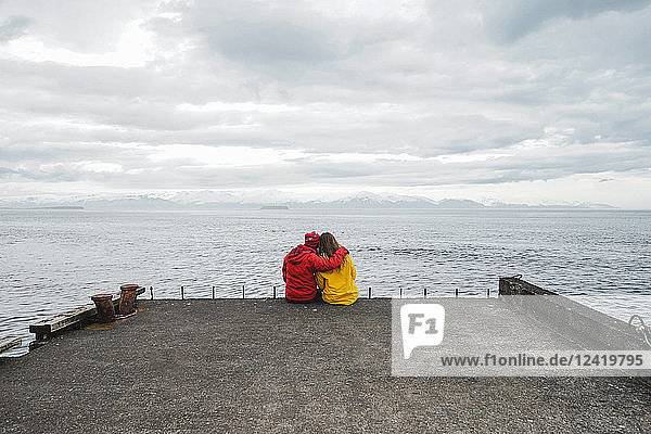 Iceland  North of Iceland  back view of couple sitting on jetty looking at view