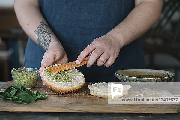 Woman preparing vegan burger  spreading avocado cream on bread roll