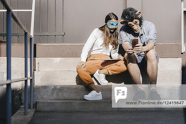 Couple in disguise sitting on stairs  using smartphone