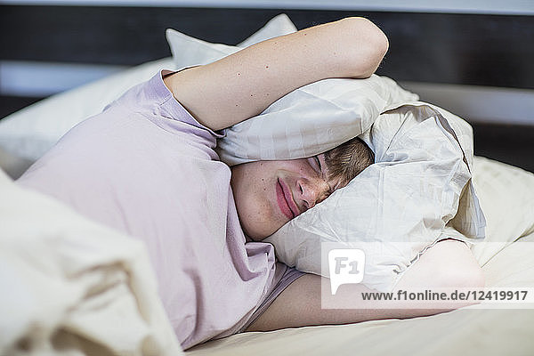 Boy lying in bed holding pillow over his head