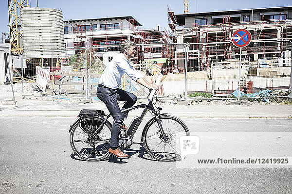 Smiling man on e-bike riding along construction site