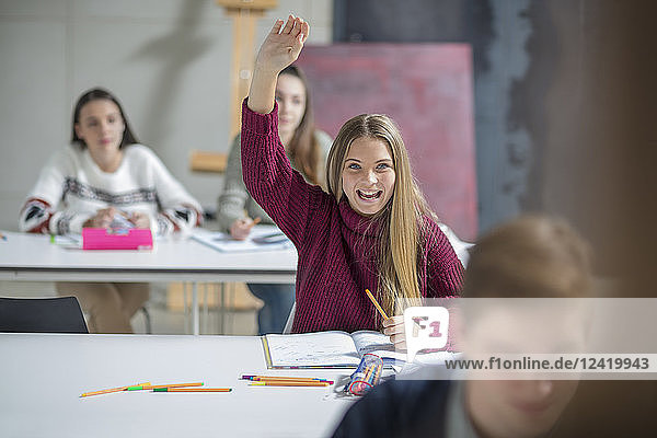 Happy teenage girl raising hand in class