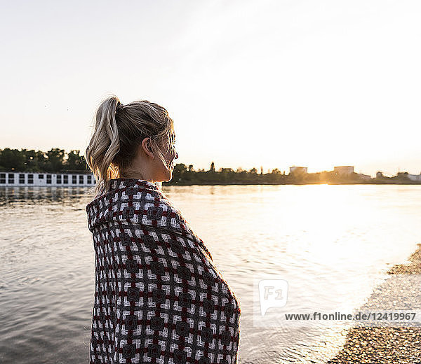 Blond woman at riverside in the evening  wrapped in a blanket
