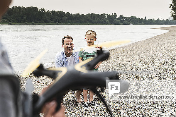 Happy father with two sons playing with drone at the riverside