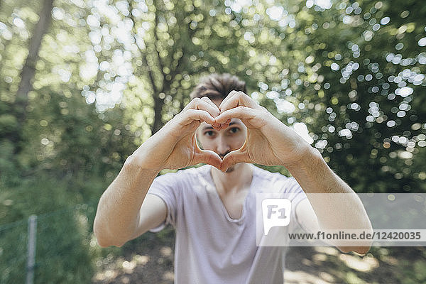 Young man making a heart with his fingers on forest path