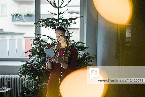 Smiling woman using tablet and headphones at Christmas time