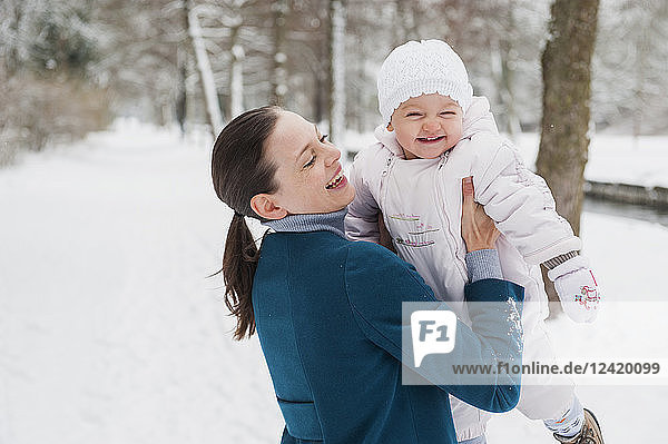 Portrait of happy baby girl having fun with her mother in snow-covered landscape