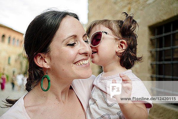 Happy baby girl wearing mother's sun glasses and kissing her