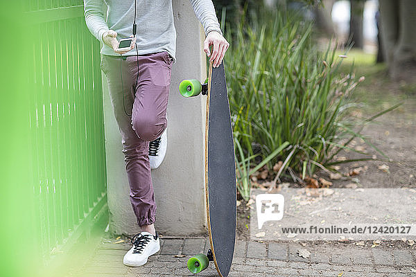 Close-up of boy holding skateboard and using cell phone