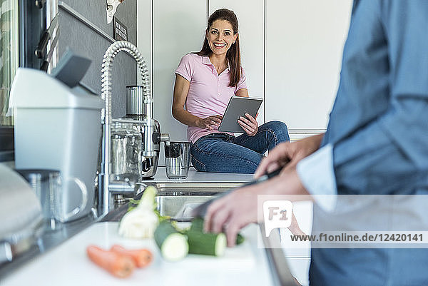 Happy couple in kitchen at home cooking and using a tablet