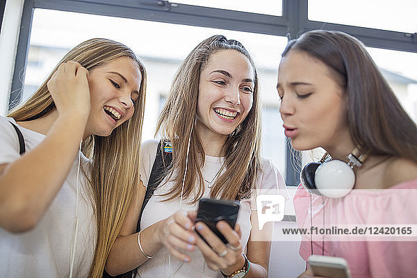 Happy teenage girls using cell phones in school