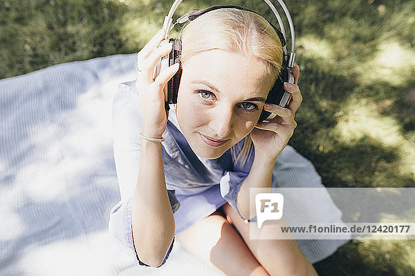 Portrait of smiling young woman sitting on blanket wearing headphones