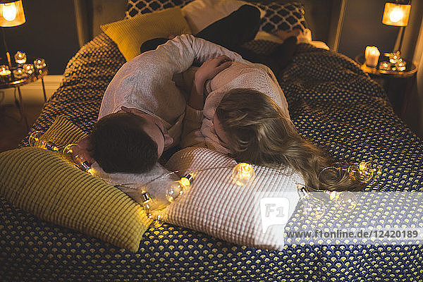 Romantic young couple cuddling in bed with fairy lights