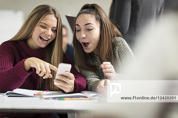 Happy teenage girls in class looking at cell phone