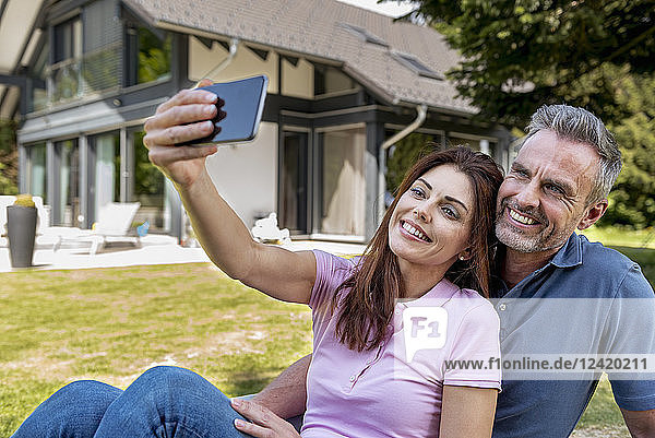 Happy couple sitting in garden of their home taking a selfie
