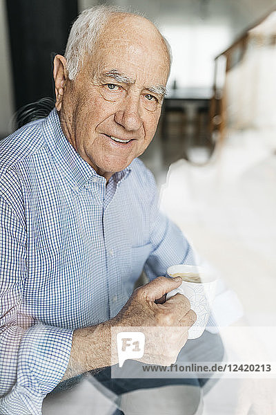 Senior man having a coffee while relaxing at home  looking at camera through a glass