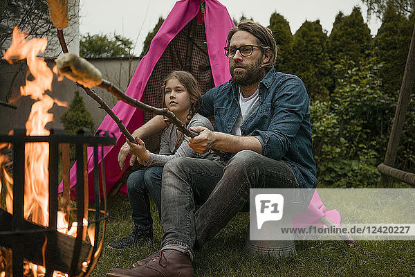Father and daughter grilling twist bread over camp fire