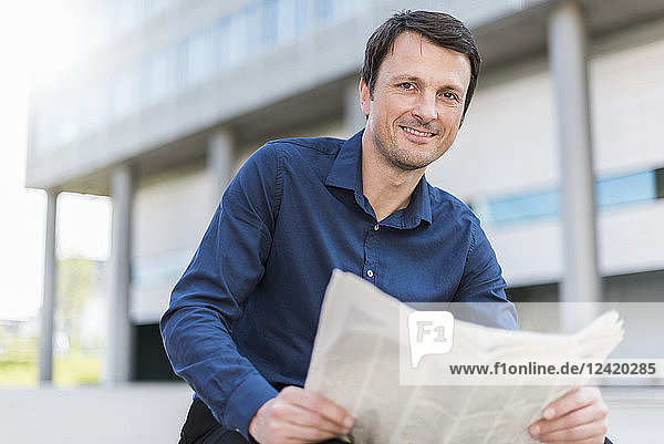 Portrait of smiling businessman with newspaper in the city