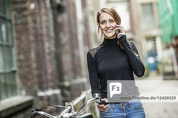 Portrait of smiling woman with bicycle on the phone