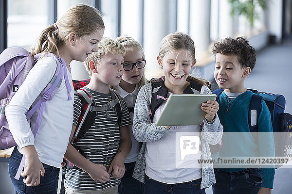 Happy pupils looking at tablet on school corridor