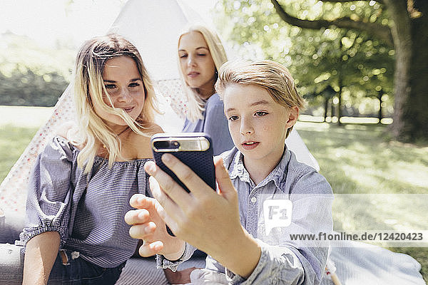 Two young women and a boy taking a selfie next to teepee in a park