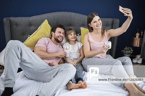 Happy family sitting on bed  taking smartphone selfies
