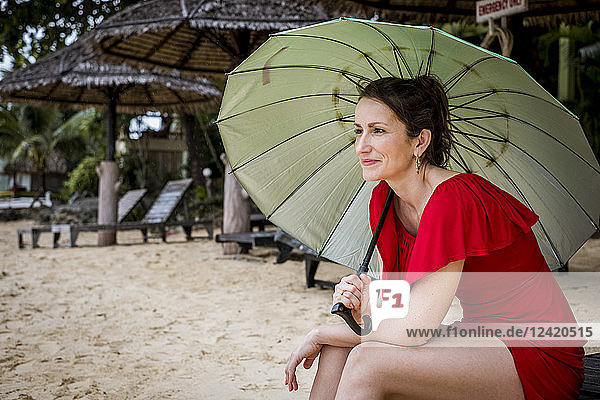 Thailand  Koh Phangan  portrait of smiling woman sitting on the beach with umbrella