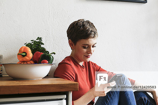 Woman sitting in kitchen  checking smartphone messages