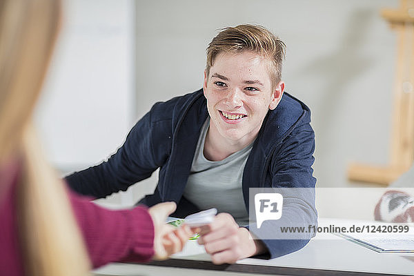 Smiling teenage boy passing a note to a girl in class