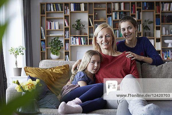 Mother and her daughters cuddling and having fun  sitting on couch