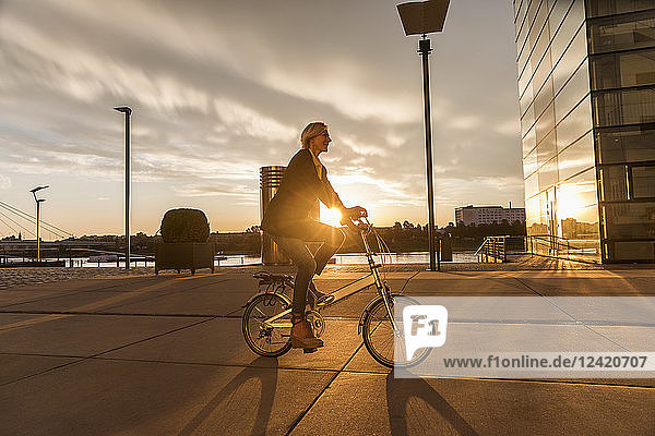 Senior woman riding city bike at the riverside at sunset