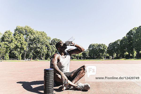 Young athlete sitting on sports field  drinking water