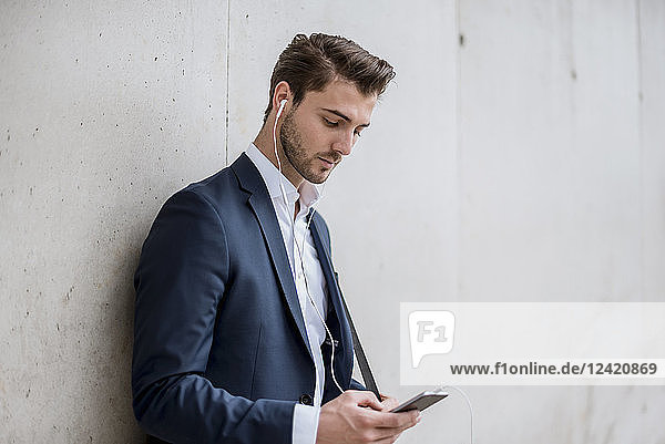 Businessman with earbuds and cell phone leaning against a wall