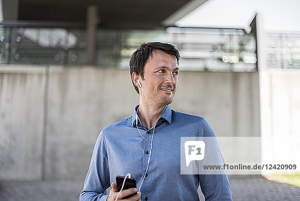 Smiling businessman with cell phone and earphones outdoors