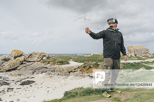France  Brittany  Meneham  man with miniature wind turbine wearing VR glasses at the coast
