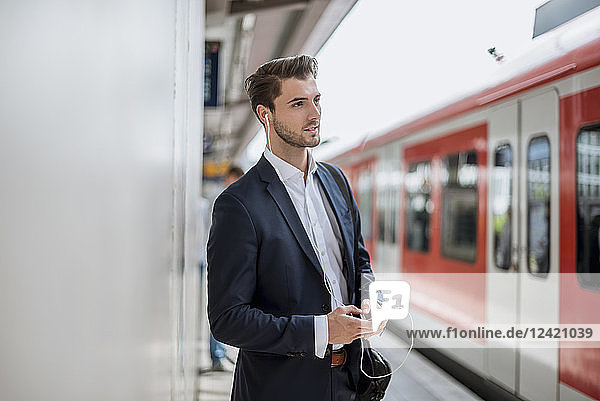 Businessman at the station with earbuds and cell phone
