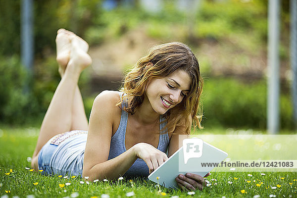 Young woman lying on meadow  using tablet