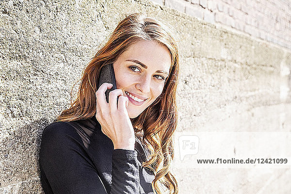 Portrait of smiling woman on the phone in front of wall
