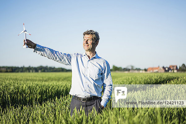 Businessman standing in grain field  holding miniature wind wheel