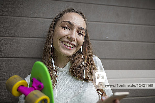 Portrait of smiling teenage girl with cell phone  earphones and skateboard