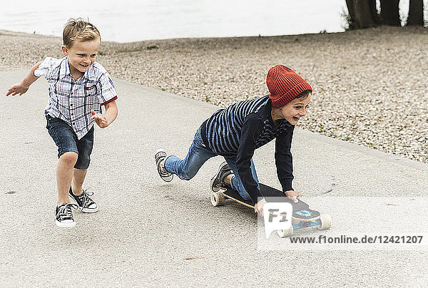 Happy boy running next to brother on skateboard